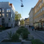 People walk down a modern city street with planters.