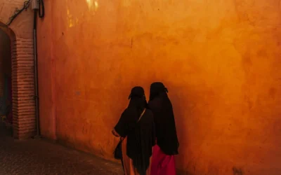 Two women in black walk down a sunlit alley.