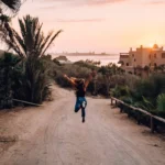 Frau springt auf einem Weg, mit Sonnenuntergang und marokkanischem Gebäude im Hintergrund.