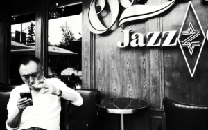 grayscale photo of man in white shirt and pants sitting on chair