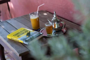 A scene in a local moroccan cafe - a tea glass, fresh orange juice, with a tea pot and a book