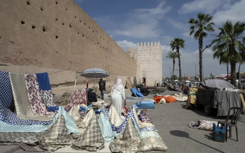 A market displays textiles in front of ancient walls.