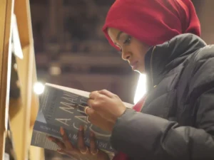 woman in red hijab headscarf and black puffer jacket reading book