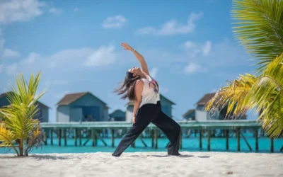 Woman practicing yoga on a sandy beach by the ocean.