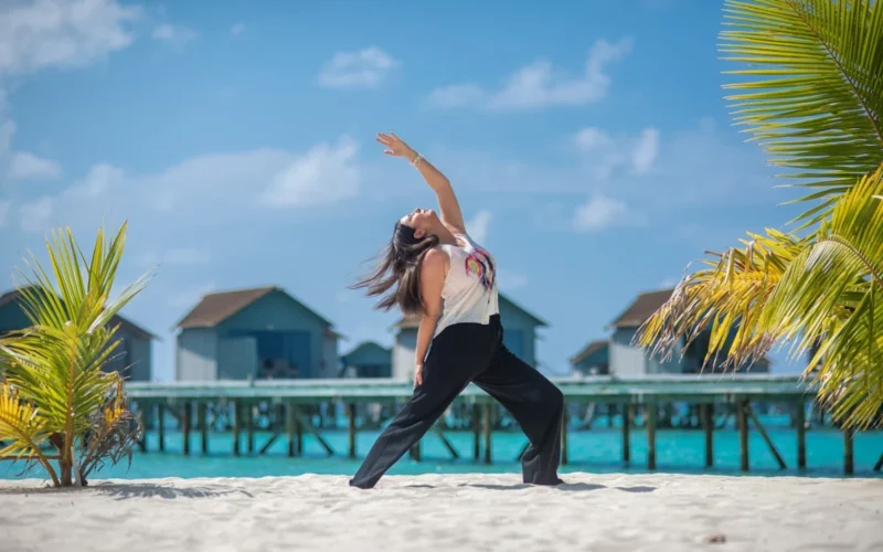Woman practicing yoga on a sandy beach by the ocean.
