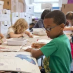 Captured in a metropolitan Atlanta, Georgia primary school, seated amongst his classmates, this photograph depicts a young African-American schoolboy who was in the process of drawing with a pencil on a piece of white paper. Note that the student was focused on a drawing book that referenced fantasy flying planes, while intent on creating his artwork, seemingly oblivious to all the classroom goings-on that surrounded him. It is important to know that objects, including pencils, crayons, paper, etc., are known as fomites, and can act as transmitters of illnesses.