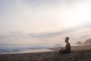 guy sits cross-legged on the beach and meditates, the wide sea in the background